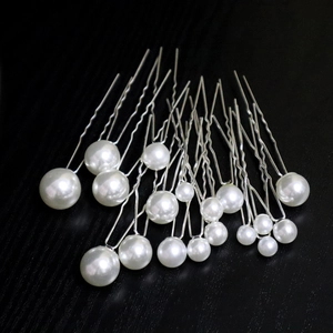 Macro detail of U-shaped hair pins with assorted sizes of white faux pearls on black surface