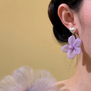 Close-up view of an ethereal purple mesh flower earring with heart stud on a model's ear