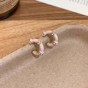 Detail view of pink enamel C-shape hoop earrings with crystal accents on a paper tray