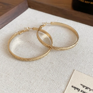Detailed close-up of gold textured hoop earrings with a matte brushed finish on wood