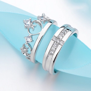 Elegant silver crown and cross couple rings set on a light blue ribbon background