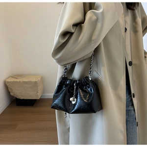 Detail of black pleated PU bucket bag with pearls on a model wearing a beige trench coat