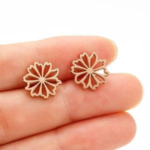 Gros plan de boucles d'oreilles fleurs ajourées en or rose tenues entre les doigts