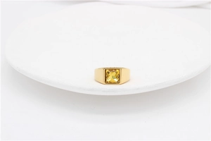 Macro shot of gold signet ring featuring a large square yellow gemstone on white stand