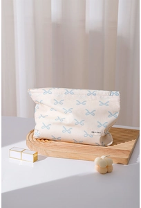 Detail view of a cream cotton makeup bag with blue bow pattern on a wooden tray