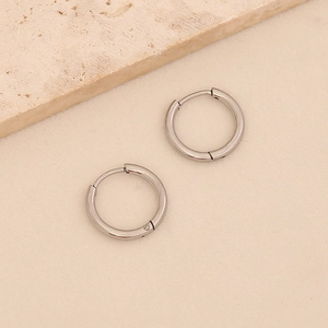 Close-up of polished silver titanium steel hoop earrings on a textured stone surface
