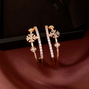 Macro shot of double-layered C-shaped gold earrings with zircon flowers on silk