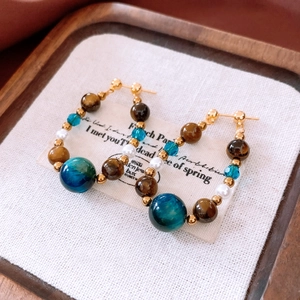 Détail de boucles d'oreilles rétro avec œil de tigre, perles et cristaux sur un plateau rustique