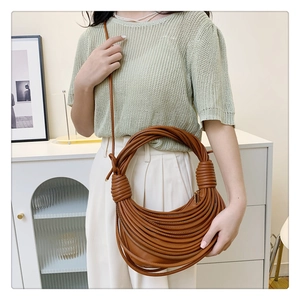 Detail of a brown crescent shoulder bag featuring intricate woven leather knot designs