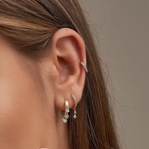 Three geometric gold earrings with cubic zirconia crystals shown on a model's ear