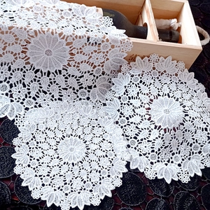 Close-up of white lace embroidery coasters and floral cotton placemats on dark surface