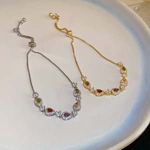 Close-up of adjustable silver and gold bracelets with colorful teardrop stones in a dish