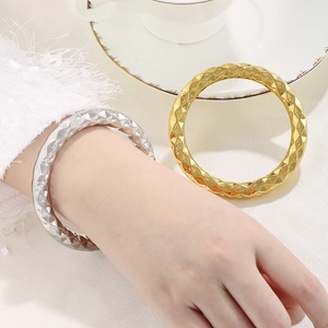 Macro detail of high-shine hollow bangles with geometric quilted pattern in gold and silver
