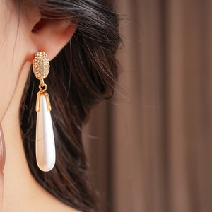 Detailed view of silver needle drop earrings with crystals and dangling white pearls