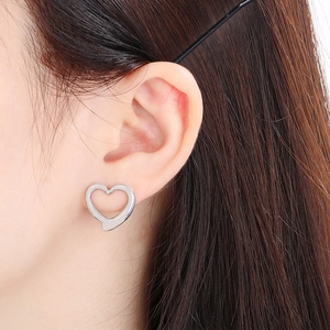 Macro shot of silver hollow heart stud earrings worn by a model in soft lighting
