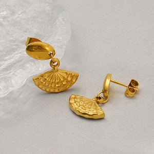 Boucles d'oreilles dorées en forme d'éventail en acier titane sur fond de tissu gris