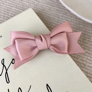 Macro shot of smooth pink satin bow hair clip with high gloss finish on vintage paper