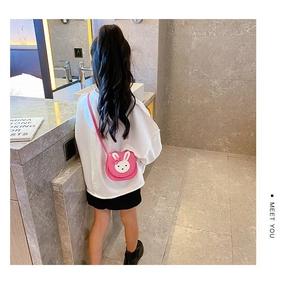 Pink cartoon rabbit mini crossbody bag shown on a child model in a modern indoor setting