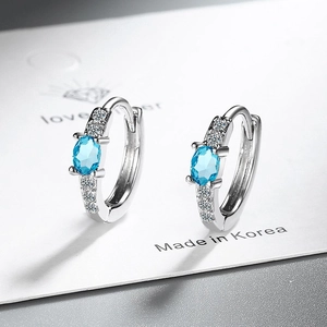 Macro detail of silver hoop earrings with oval blue stone and sparkling zircon accents