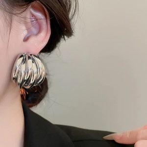 Close-up of chunky twisted silver metal earrings with a polished mirror finish on model