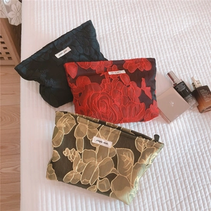 Detail of embossed floral toiletry bags in black, red, and green with a zipper closure