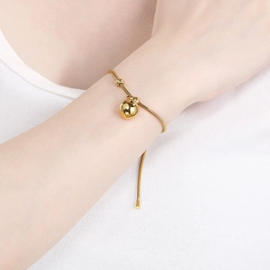 Detail eines verstellbaren Goldkugel-Anhängers an einem Schlangenkettenarmband am Handgelenk