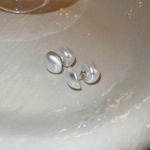 Close-up of matte silver geometric earrings with lustrous white pearls on a textured base