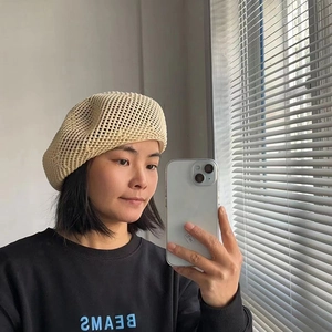 Close-up of beige knitted hollow beret hat with handmade texture and breathable design