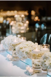 Detail van drijvende kaarsen in glazen cilinders met witte bloemen en sfeerverlichting