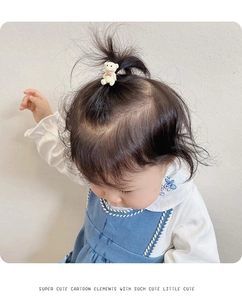 Detail of cream bear hair tie with red bow worn by child in blue suspender dress
