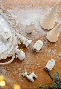 Set of white ceramic Christmas tree ornaments with gold trim on a snowy wooden background