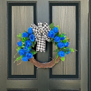 Blue faux rose Christmas wreath with black and white plaid bow on a rustic wooden door