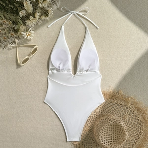 Flat lay of a white plunging neck monokini with straw hat and sunglasses for summer travel