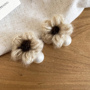 Detail of beige knitted flower earrings with brown centers and round white pearls