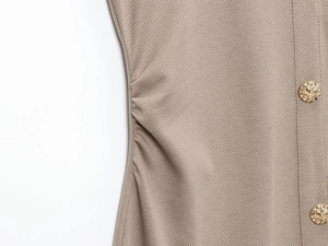 Detail eines khakifarbenen Strickkleides mit seitlicher Raffung und Goldknöpfen