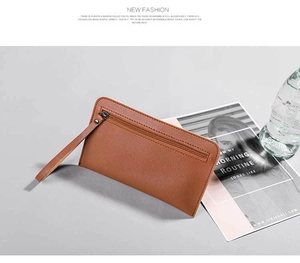 Brown litchi grain leather clutch bag with metal zipper and wrist strap on a modern desk