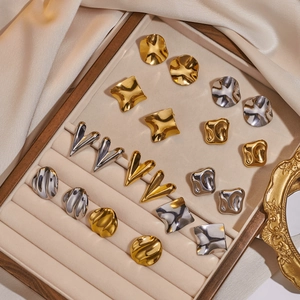 Sammlung unregelmäßiger geometrischer Gold- und Silberohrstecker auf beigem Samtdisplay