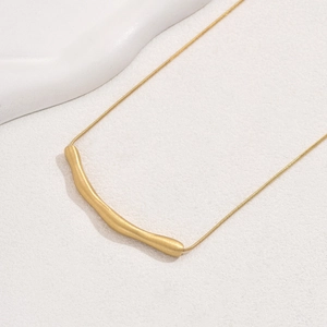 Dettaglio del ciondolo a tubo curvo oro opaco su una sottile catena dallo stile minimalista