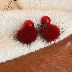 Detail of red plush faux fur ball earrings on white knit fabric for autumn and winter