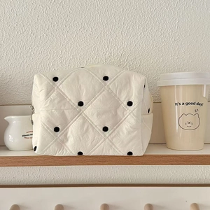 Détail de la trousse de maquillage matelassée crème à pois noirs sur étagère