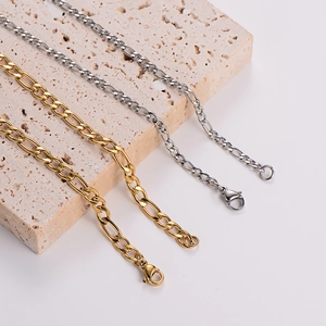 Detailed close-up of gold and silver Figaro chain necklaces on a beige stone