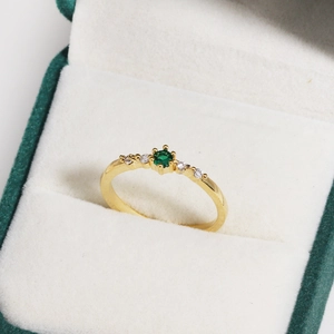 Detail of gold-plated ring with round green zircon and side crystals in jewelry box