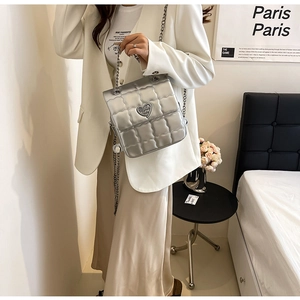 Detail of silver quilted handbag with metal chain strap and heart shaped buckle on model