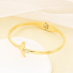Detailed shot of a gold fishtail bangle with zircon on a soft beige background