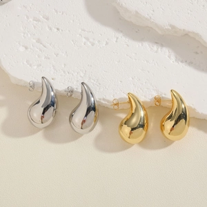 Polished teardrop earrings in gold and silver finish on a natural stone display