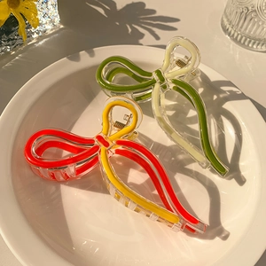 Detail of jelly-colored bow hair claws with gold springs in a ceramic tray