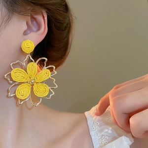 Detail shot of a woven raffia flower earring with gold metal frame worn by a model