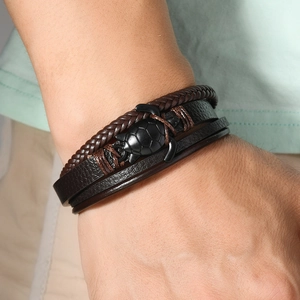 Detail eines mehrlagigen braunen und schwarzen Lederarmbands mit Schildkrötenanhänger