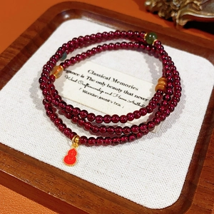 Macro detail of multi-layer garnet bead bracelet with a golden-edged red gourd pendant