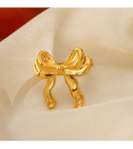 Macro view of 18K gold plated stainless steel bow ring on elegant beige velvet